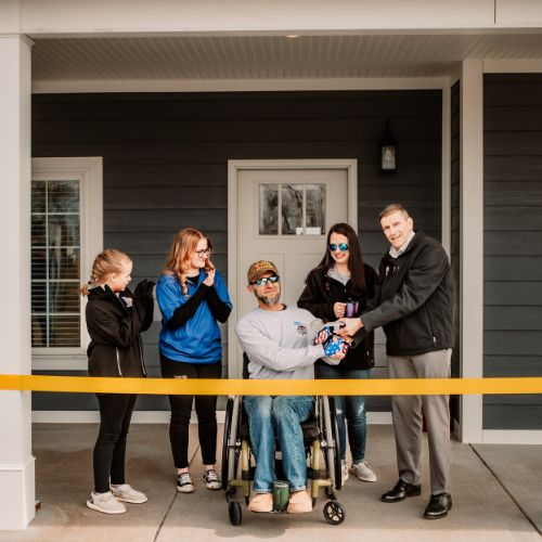 Photo of a Veteran cutting the ribbon with his family to their new HFOT House
